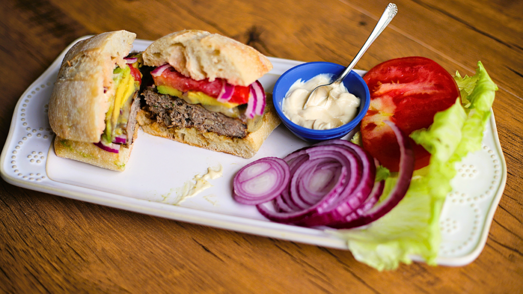 turkey burger cut in half on white tray with red onion, tomato, avocado