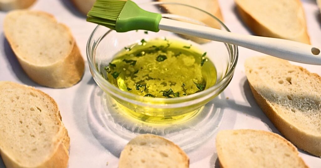 extra virgin olive oil in small dish with sliced baguette on cookie sheet