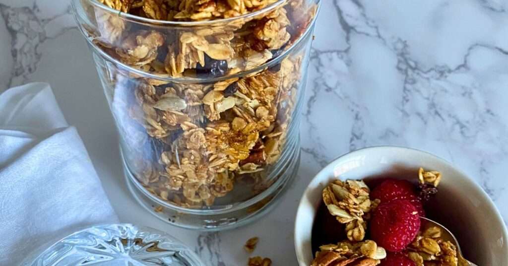 granola in a glass jar with raspberries in a small ramekin next to it