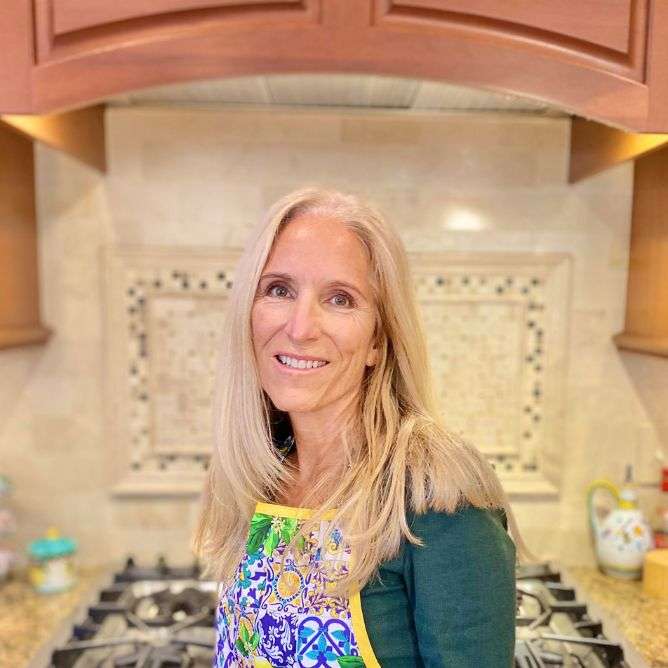 Rebecca next to cooktop wearing colorful blue, yellow and green print Italian apron